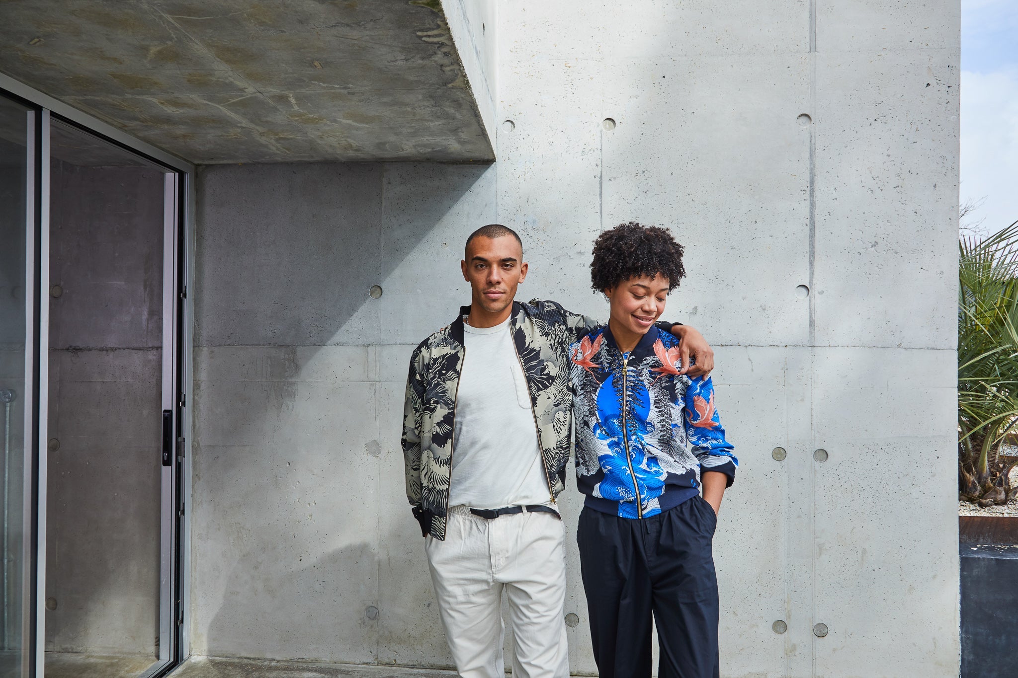 A man wearing a silk bomber jacket with his arm around a woman wearing a silk bomber jacket