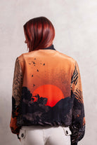 A person viewed from the back wearing a peach silk bomber jacket with a geometric pattern featuring a sunrise motif.