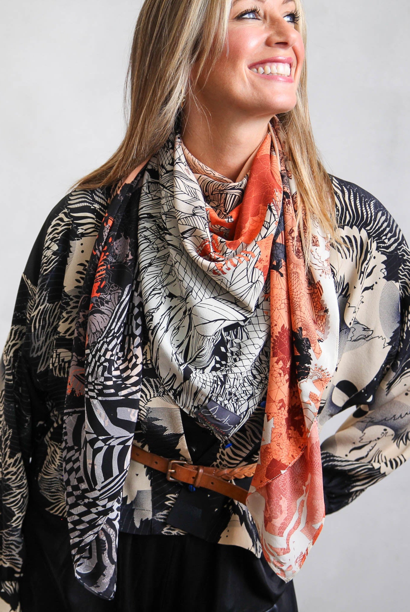 Wman smiling, wearing peach silk scarf and monochrome silk shirt.