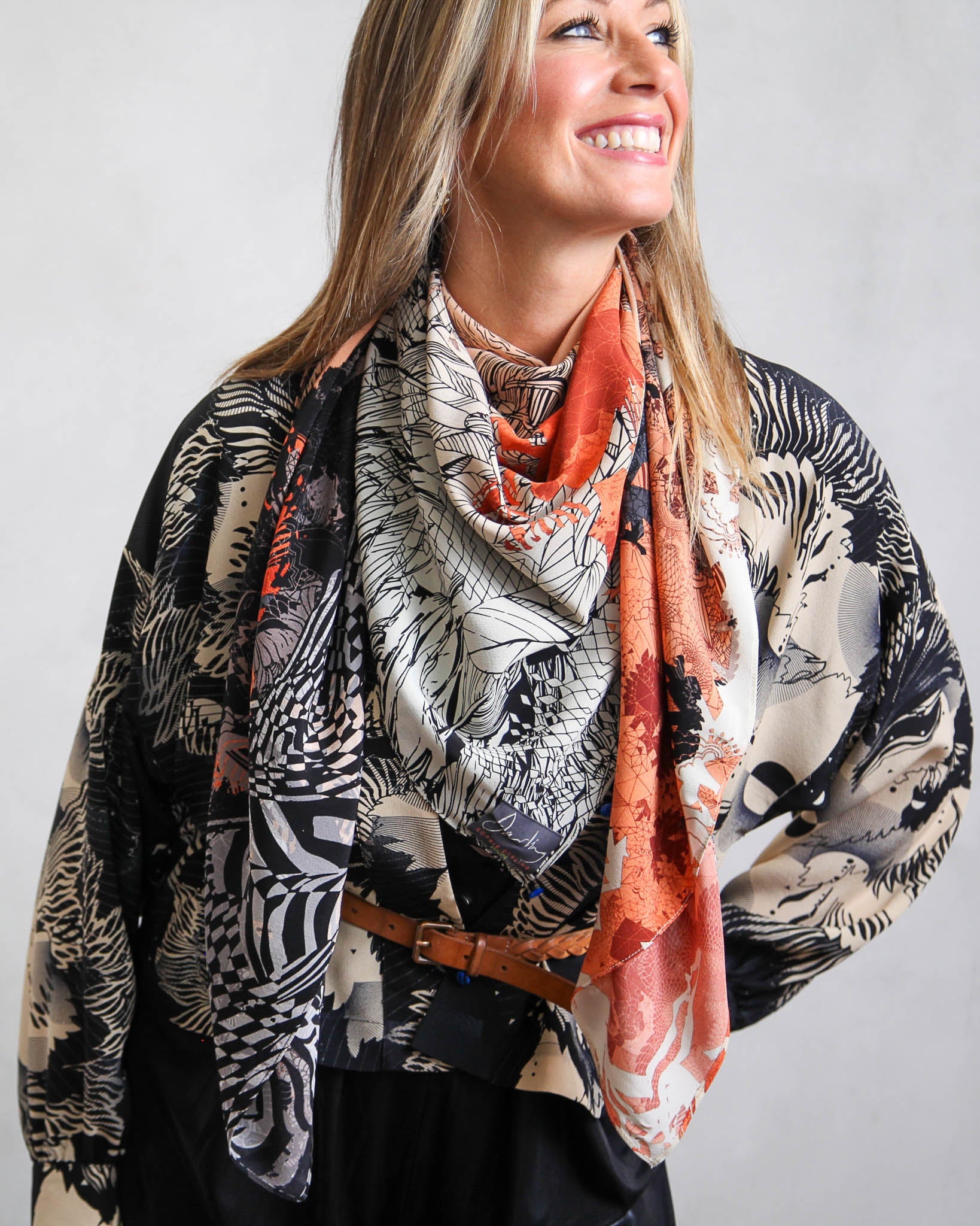 Wman smiling, wearing peach silk scarf and monochrome silk shirt.