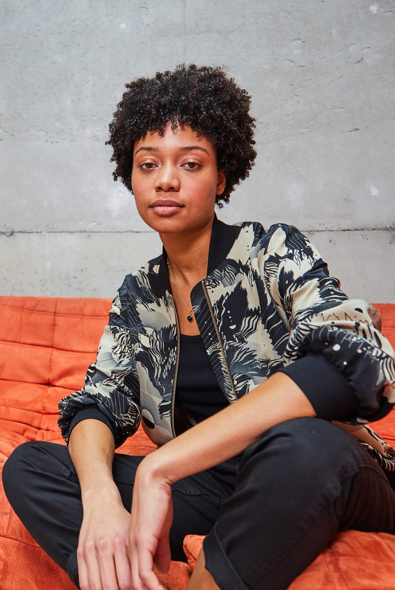 A woman wearing a printed silk bomber jacket in grey and cream geometric floral design