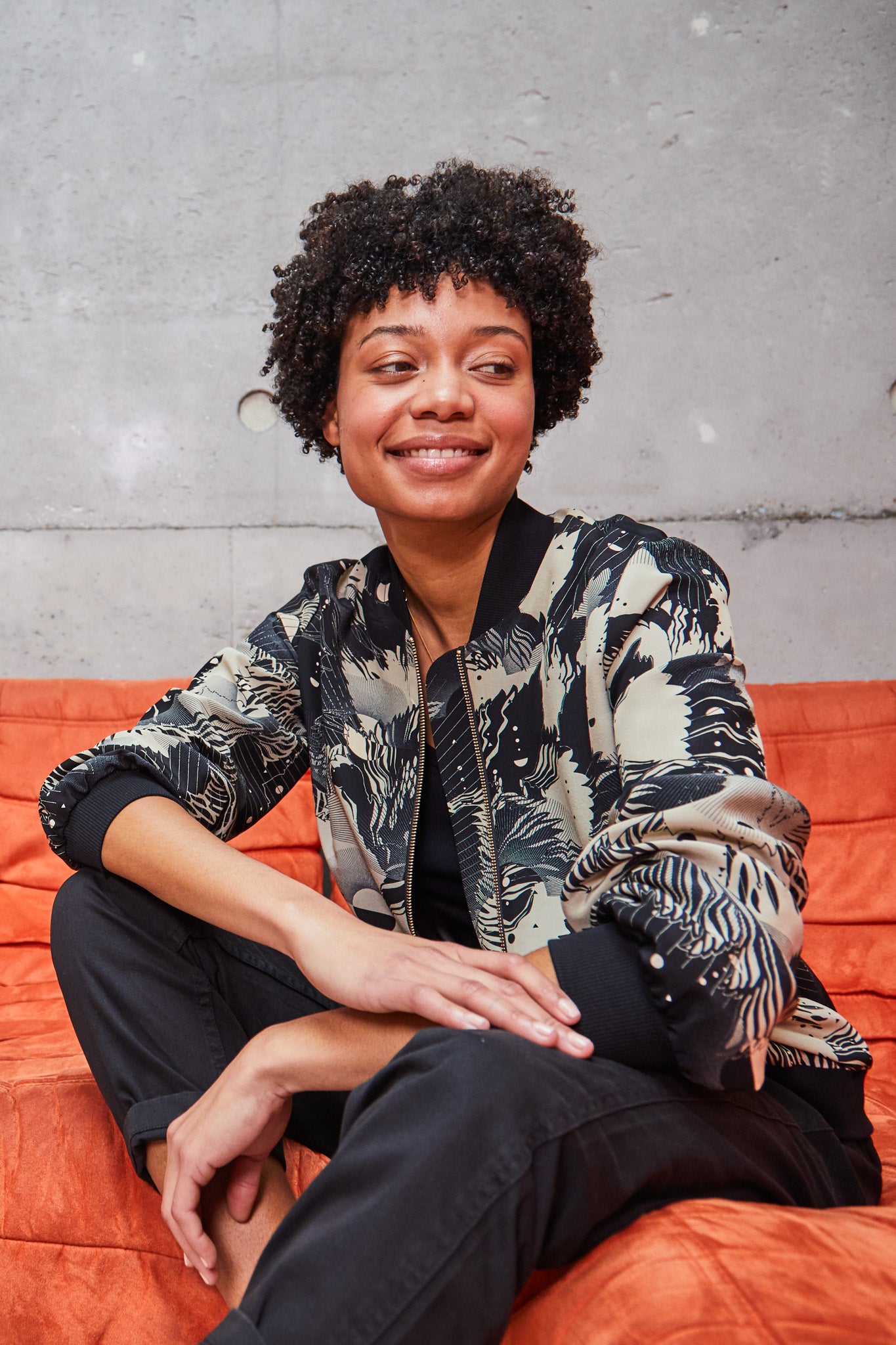 A woman wearing a printed silk bomber jacket in grey and cream geometric floral design