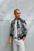 A man wearing a silk mens bomber jacket in a deep navy and cream print abstract floral print