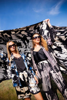 Two women holding a large black and white patterned fabric against a blue sky.