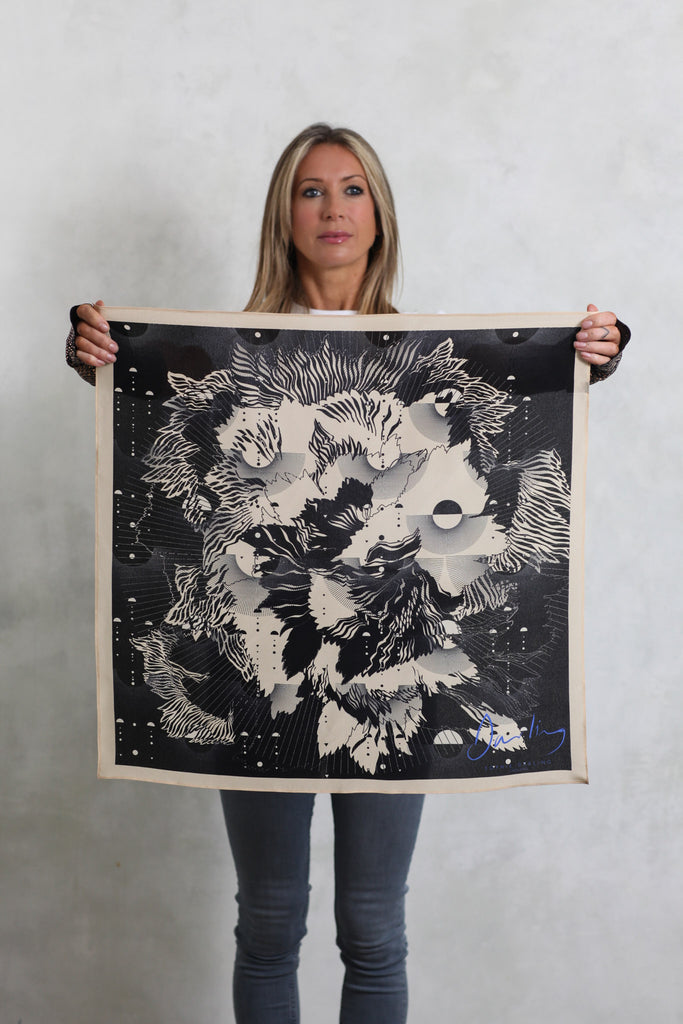 A woman holding a silk scarf with an abstract floral design in cream and black.