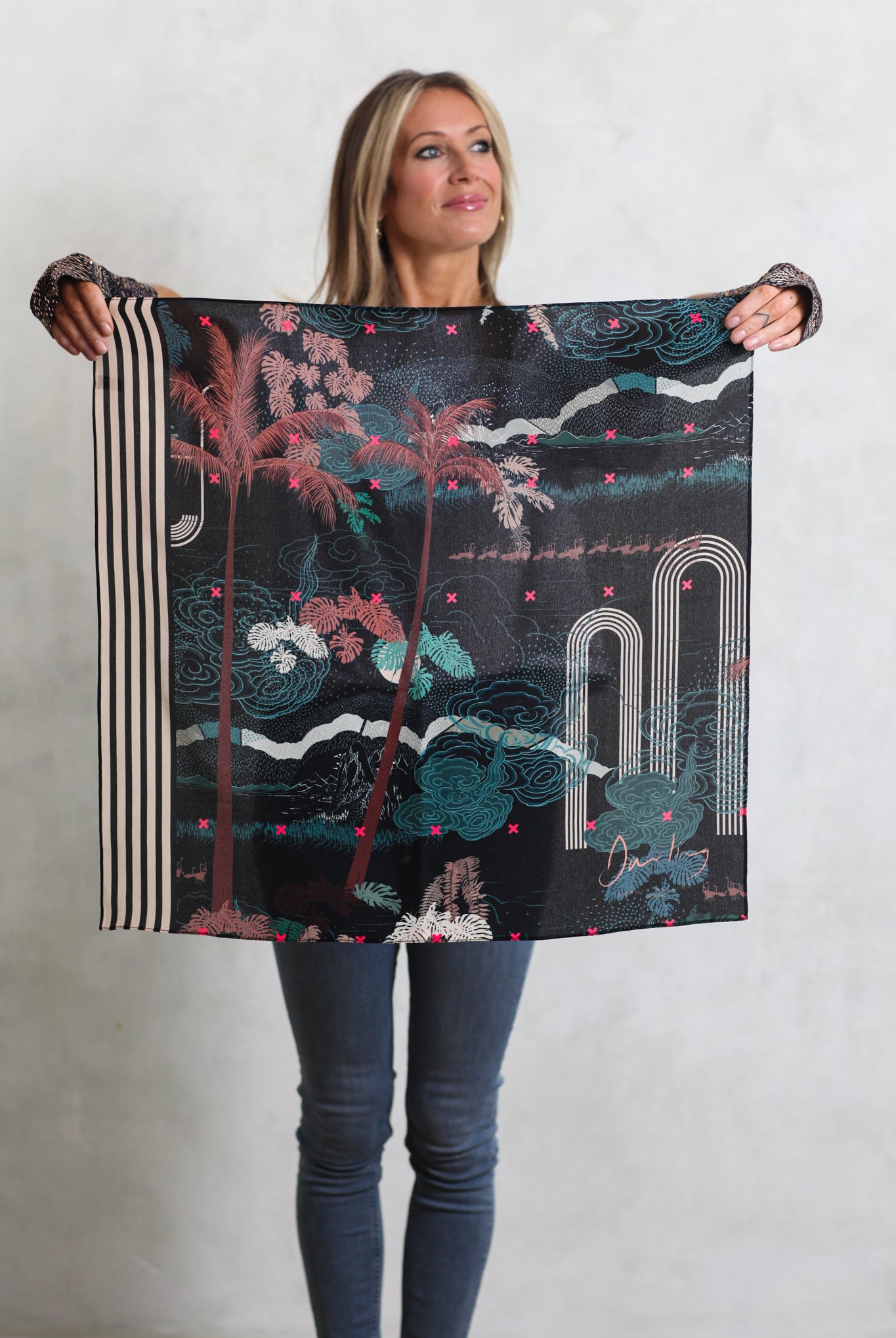 A woman holding a silk scarf with a tropical design in blacks, greens and pinks