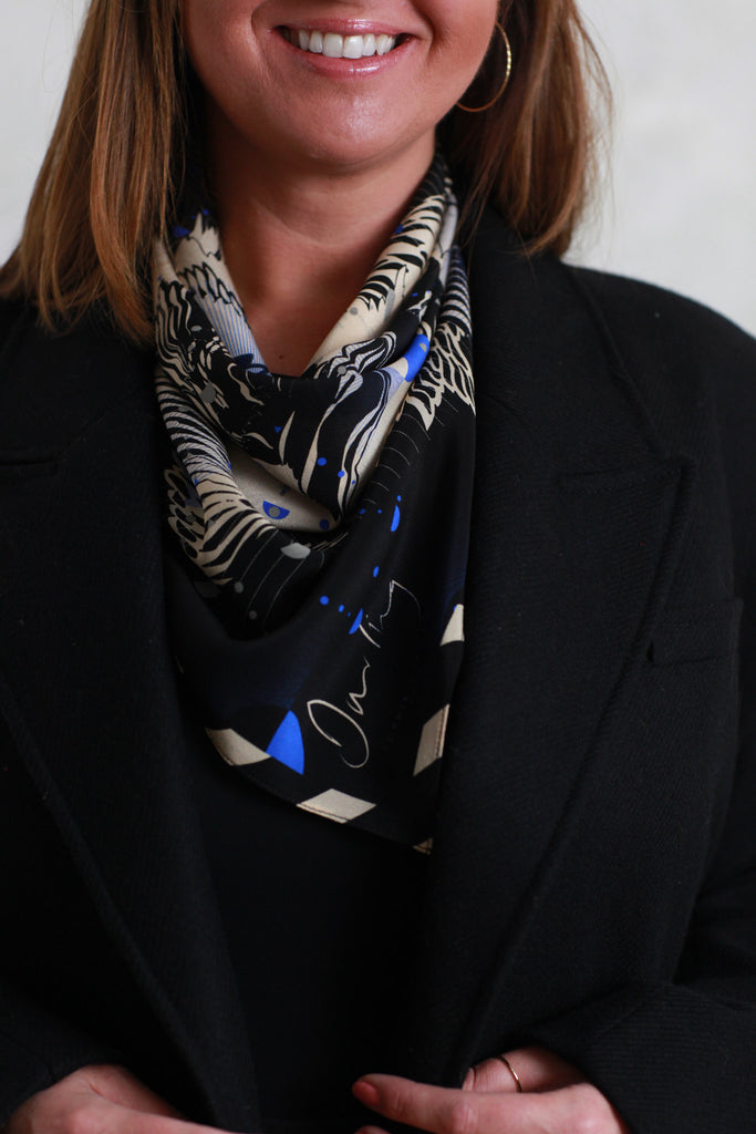 A woman wearing a silk scarf around the neck with a abstract floral design in cream and navy blue