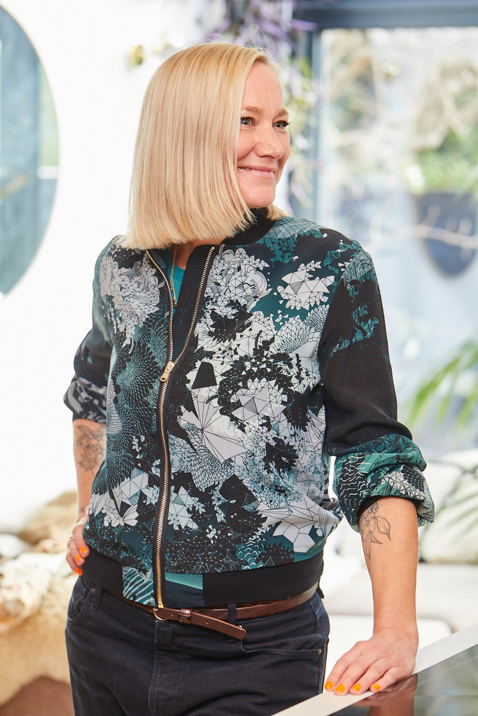 A woman wearing a silk bomber jacket with intricate geometric patterns in blues and white