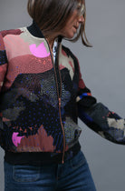 A woman wearing a silk bomber jacket in black and pink with a landscape design and bright pink suns 