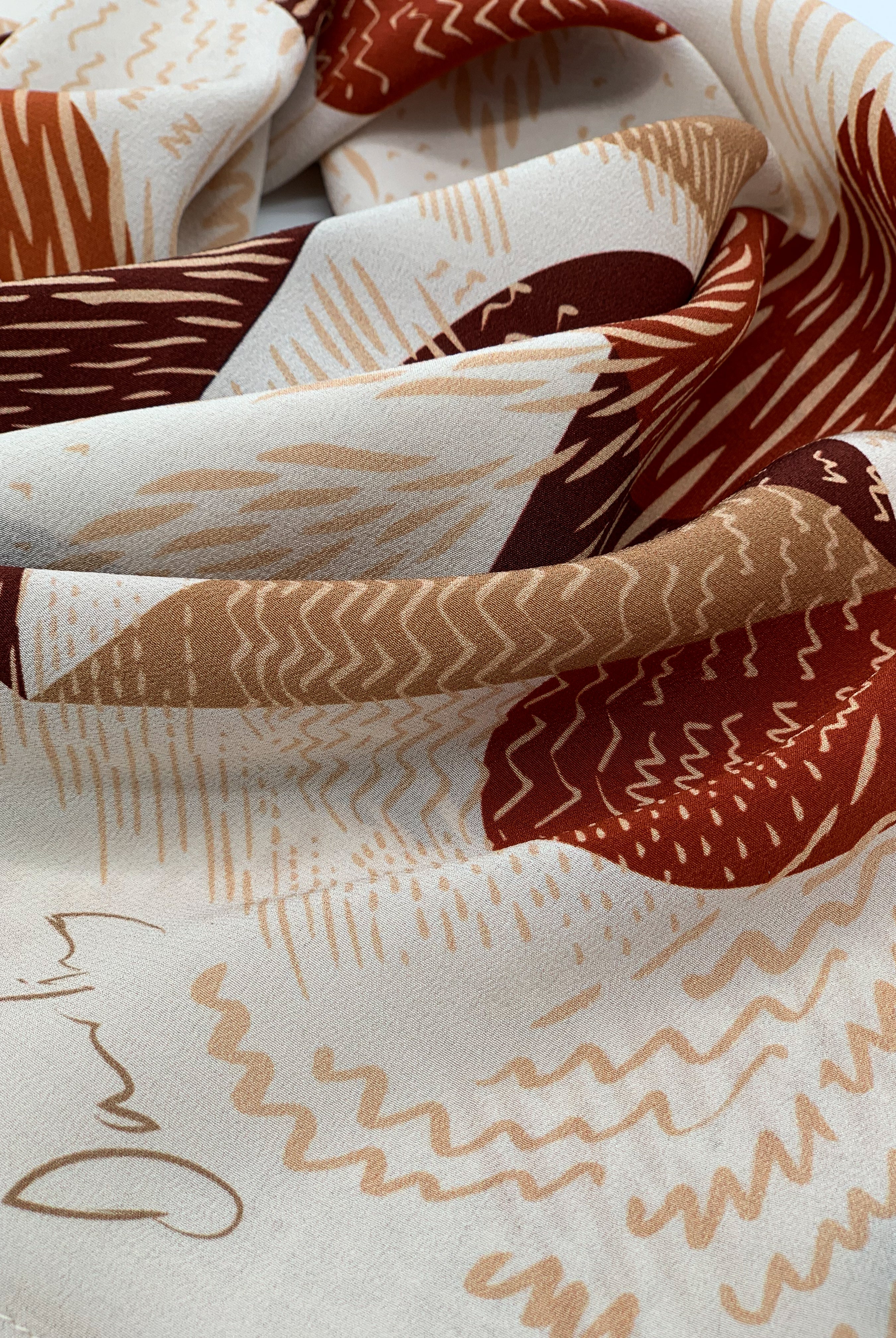 A close up of a silk printed scarf in earthy tones