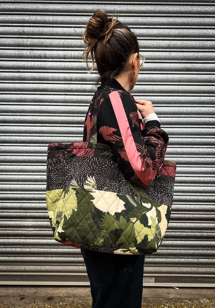 A woman wearing a quilted tote bag with a striped print in green camouflage with green stalks 