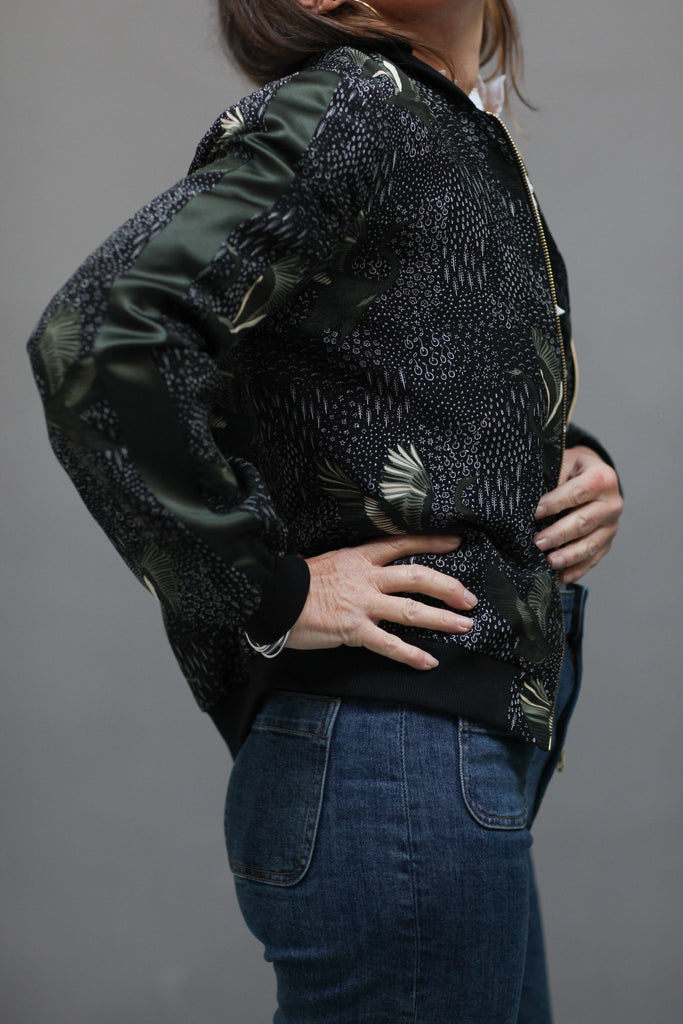 A woman wearing a printed silk bomber in green and black