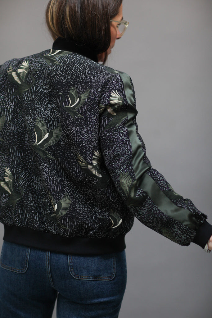 A woman wearing a printed silk bomber in green and black