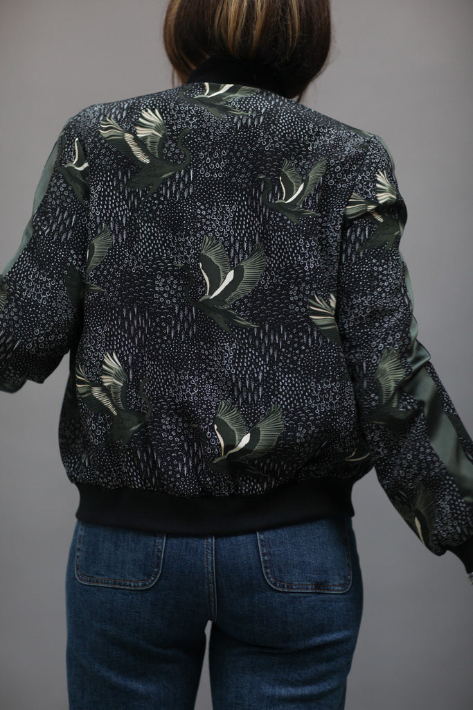 A woman wearing a printed silk bomber in green and black