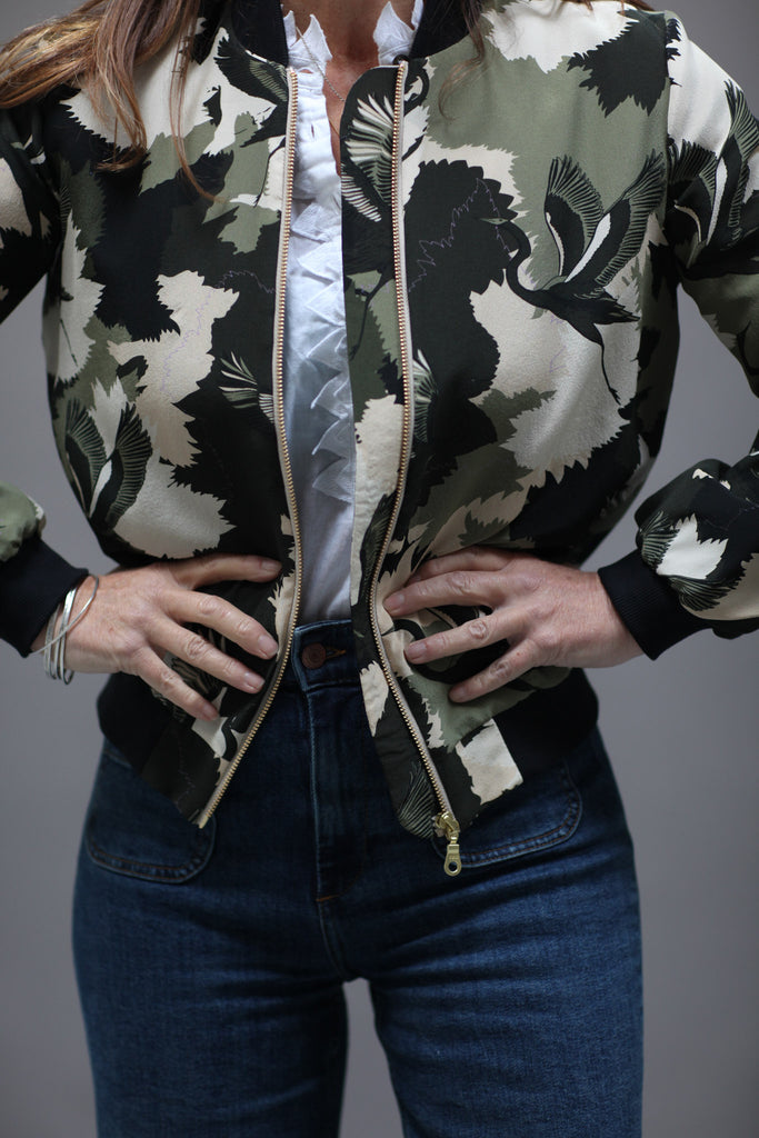 A woman wearing a printed silk bomber jacket in greens and cream camouflage print with stalk details