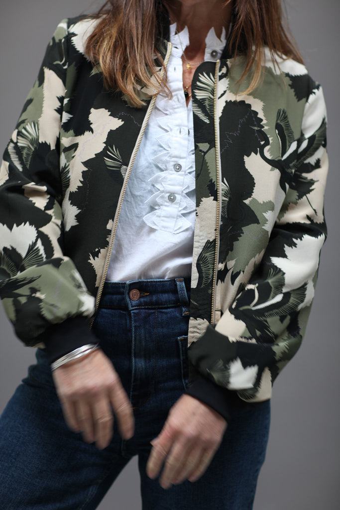A woman wearing a printed silk bomber jacket in greens and cream camouflage print with stalk details