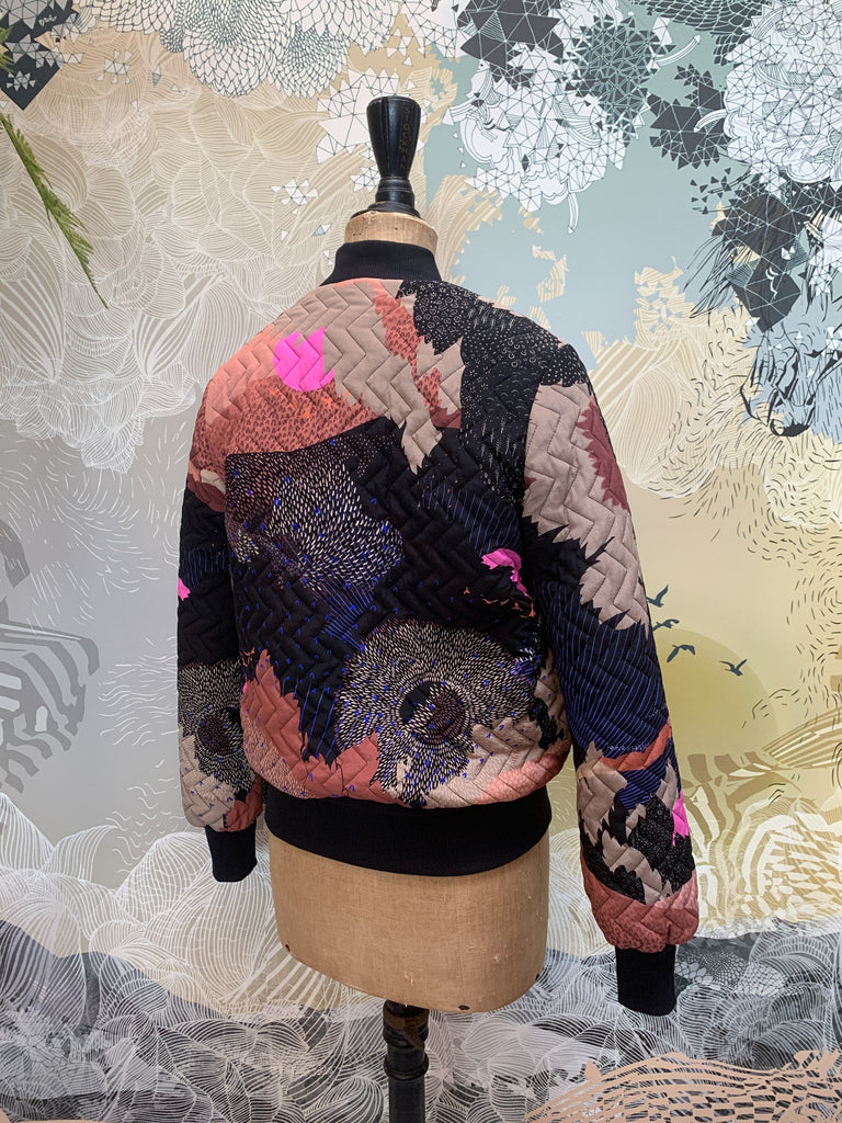 The back of a quilted silk bomber jacket in blacks, pinks with abstract shapes and bright pink suns