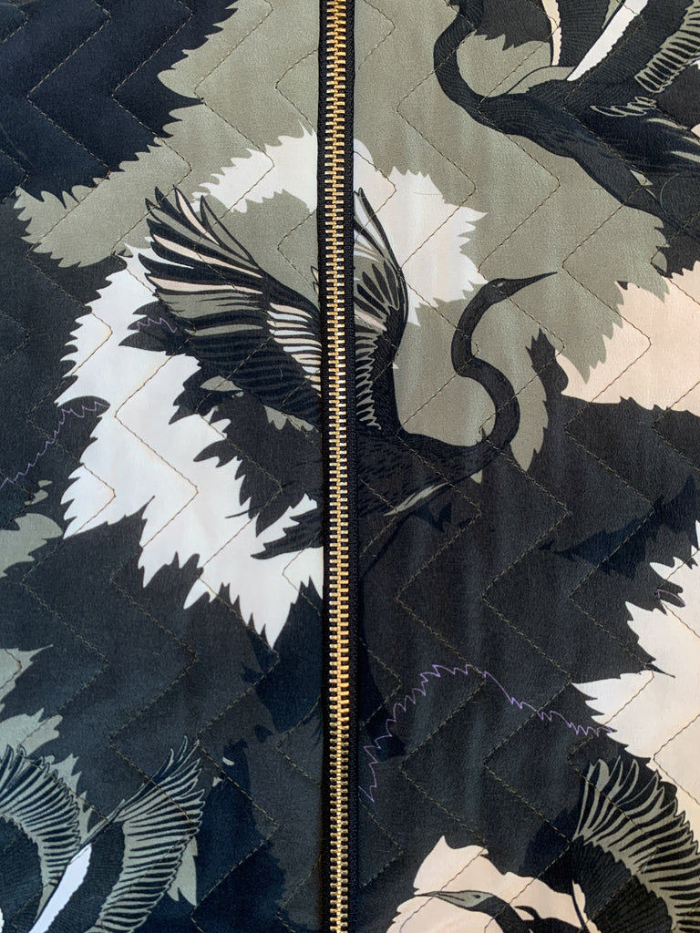 A close up of a zip on a quilted silk bomber jacket in a green and white camouflaged print 