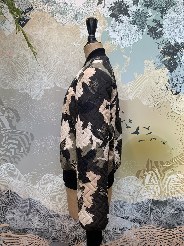 A side view of a quilted silk bomber jacket in a green and white camouflaged print 