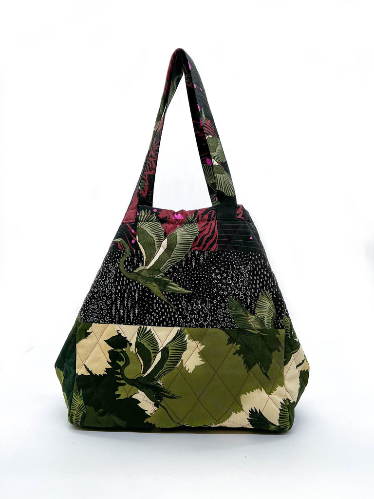 A quilted tote bag with a striped print in green camouflage with green stalks and maroon background 