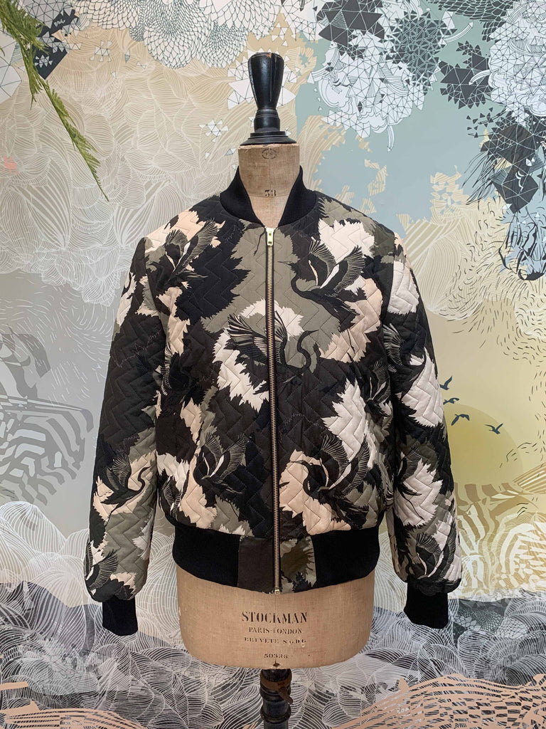 A mannequin image of a quilted silk bomber jacket in a green and white camouflaged print 