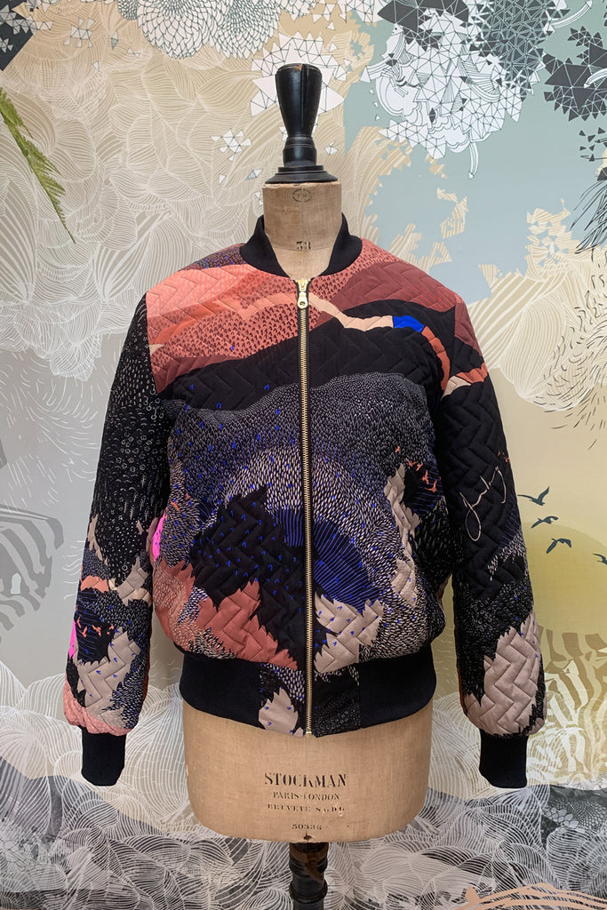The front of a quilted silk bomber jacket in blacks, pinks with abstract shapes and bright pink suns