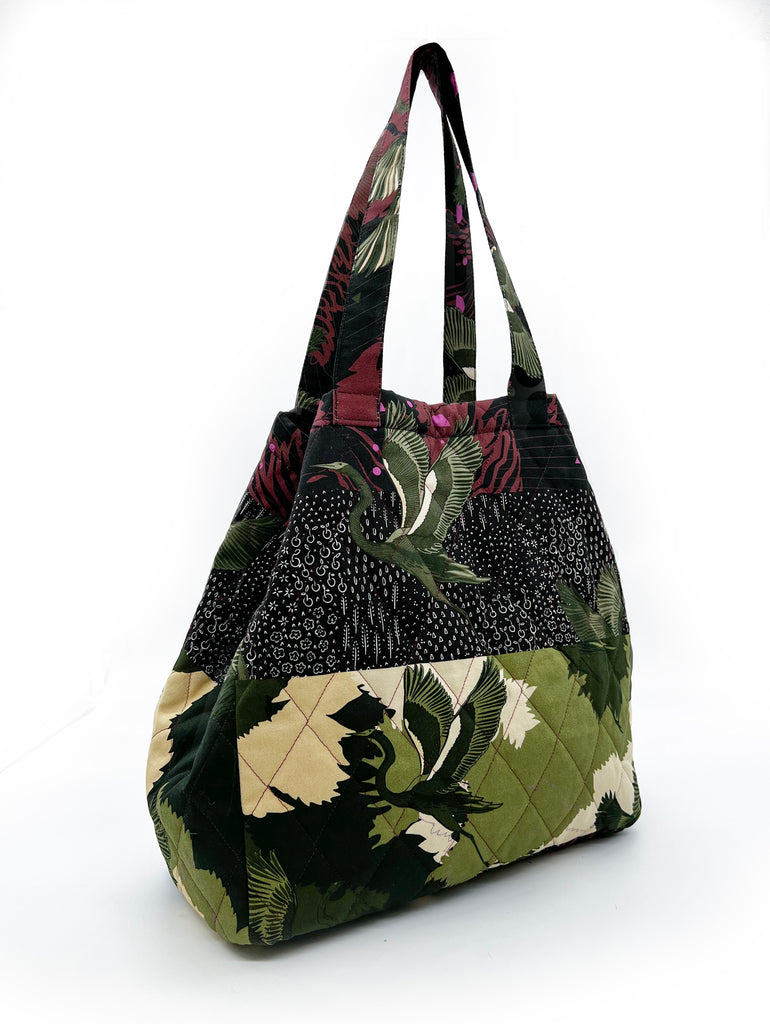 A quilted tote bag with a striped print in green camouflage with green stalks and maroon background 