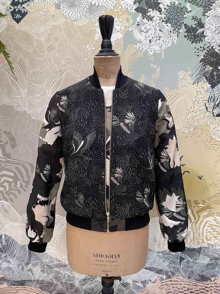 The front of a silk bomber jacket unzipped in shades of green with a camo and a stalk design