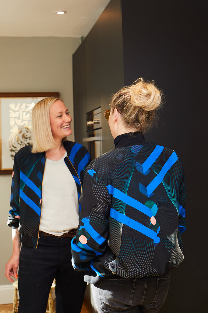 Two women wearing a Silk Bomber Jacket's with bold blue stripes, geometric lines and pink circles