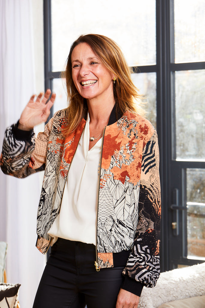 Woman wearing a Sophie Darling Sunrise silk bomber jacket in orange and black with sunrise design