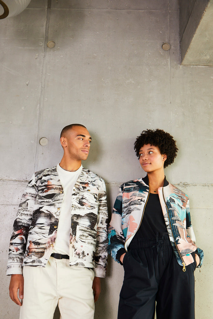 A woman leaning on a wall wearing a silk bomber jacket in green, coral and browns 