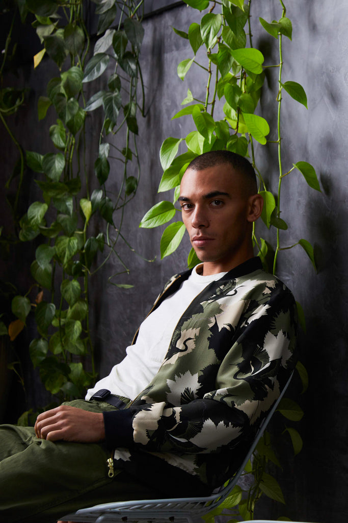 A male wearing a silk mens bomber jacket in a cream and green camouflage print with a stalk design