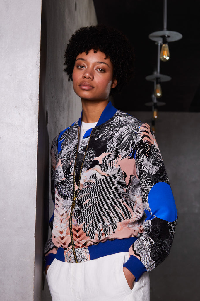 A woman wearing a silk bomber jacket in blue, pink and monochrome tropical print