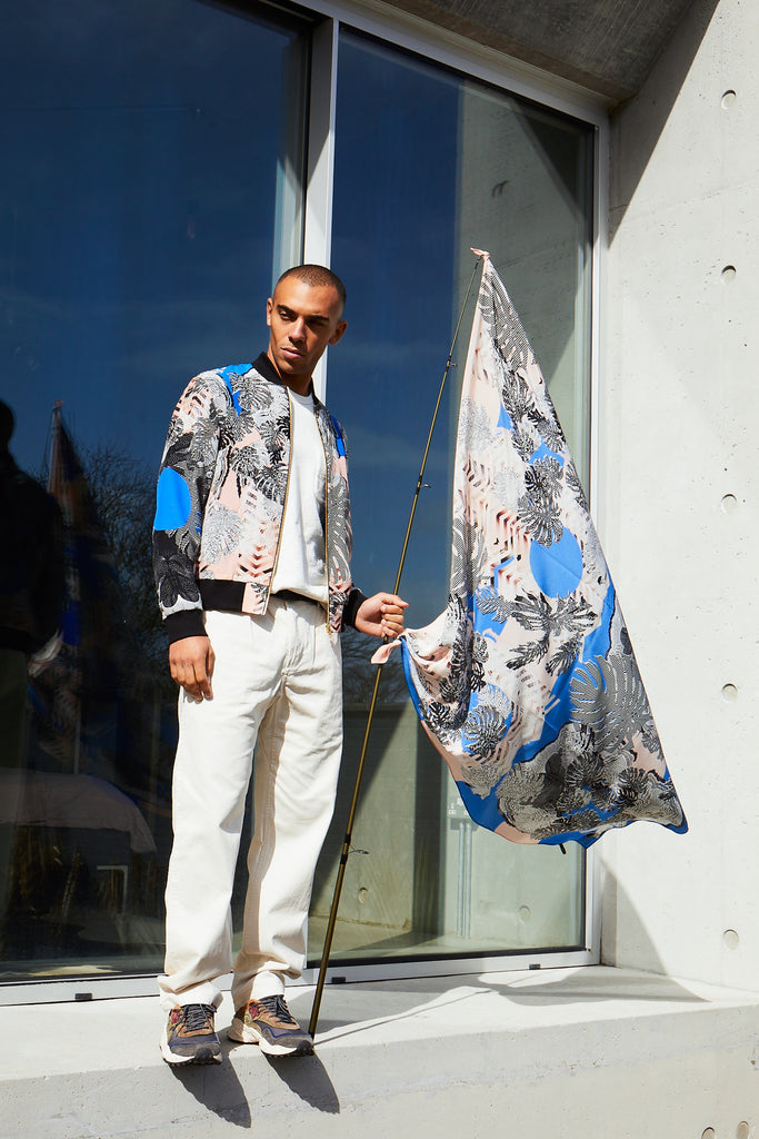 A man wearing a Mens Bomber Jacket in pink and blue featuring a monochrome tropical leaves design