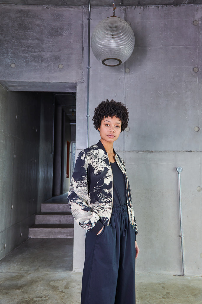 A woman wearing a printed silk bomber jacket in a navy and cream abstract floral and geometric print