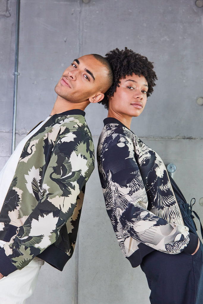 A man and woman leaning on each other wearing silk bomber jackets in camo and abstract floral