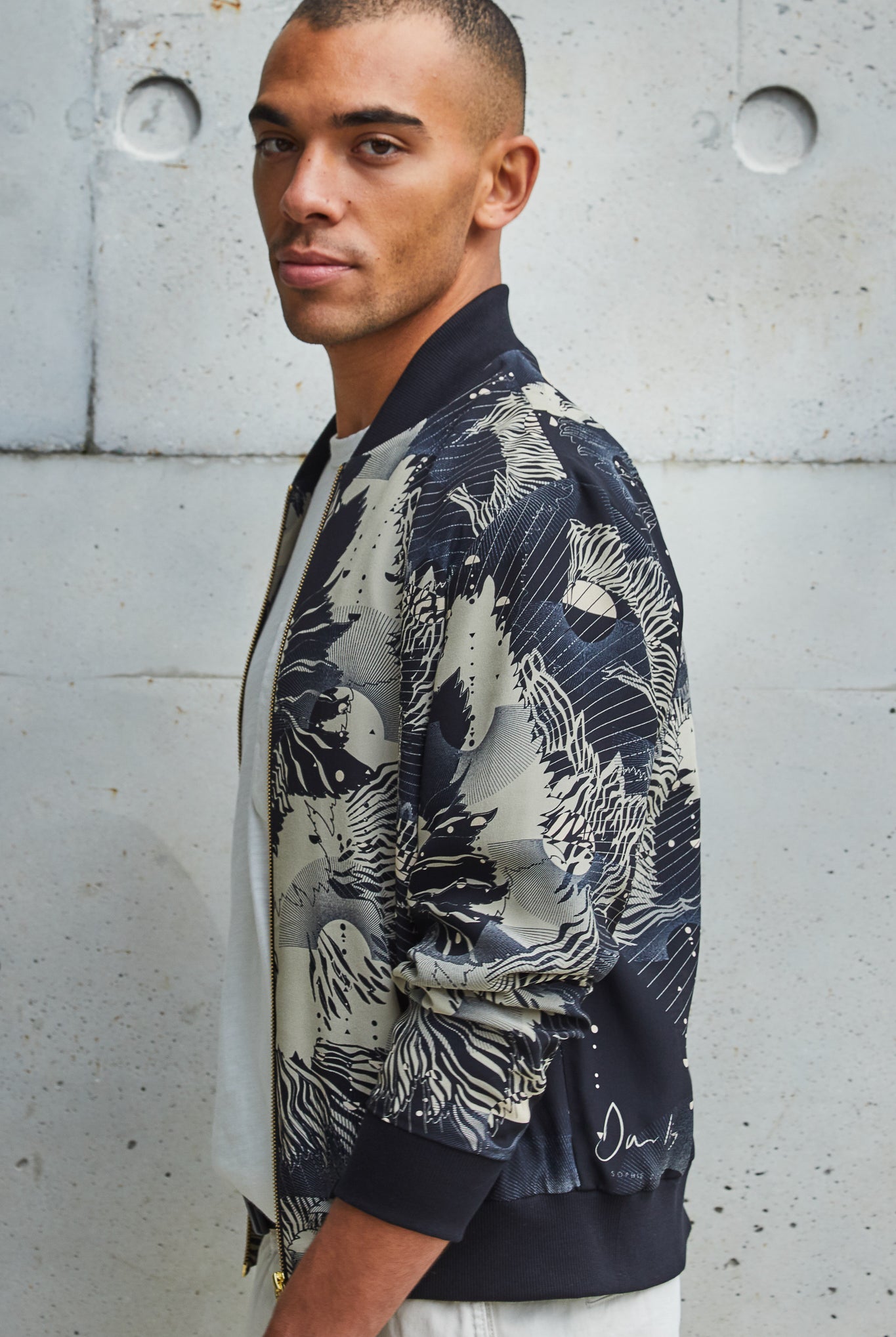 A man wearing a silk mens bomber jacket in a deep navy and cream print abstract floral print