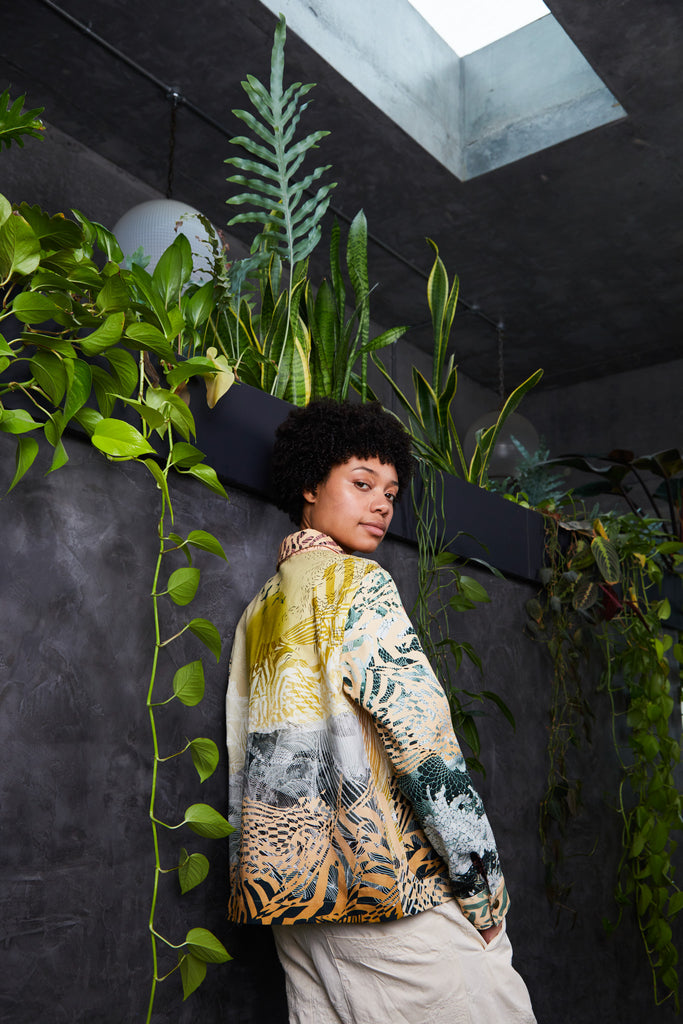 A woman wearing a Cotton Utility Jacket in muted yellows with a mountain landscape and sun design
