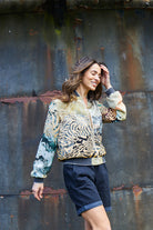 Women wearing silk bomber jacket in muted yellows and greens with a mountain landscape 