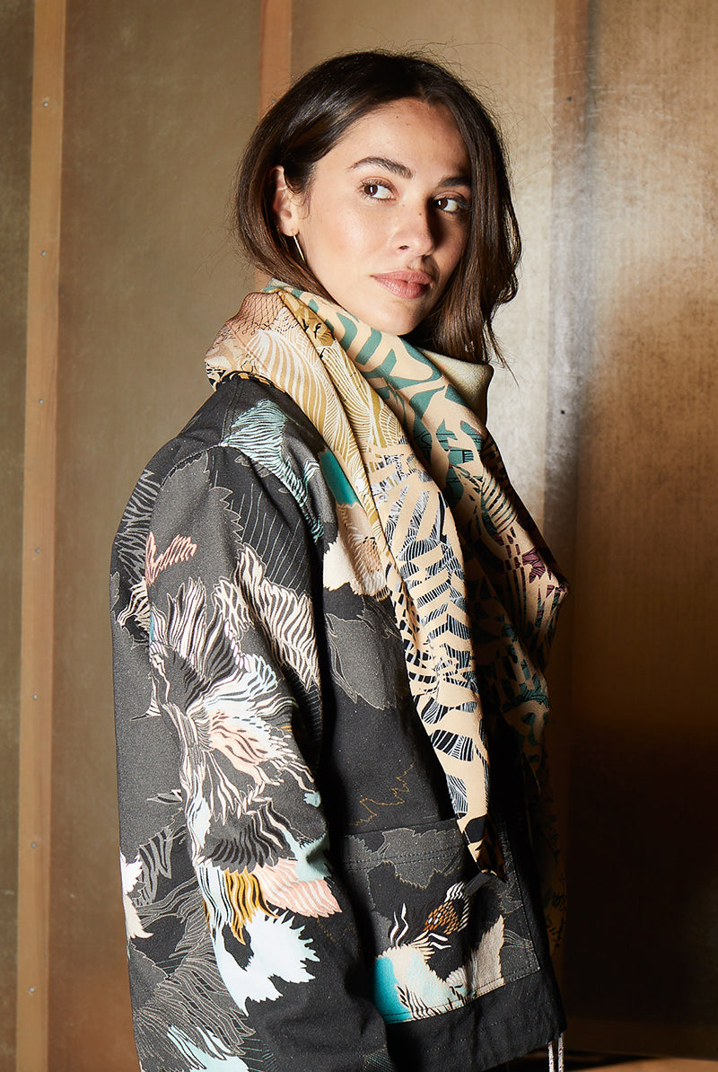 A model wearing a silk scarf with a sunrise design in muted yellows, greens and coral