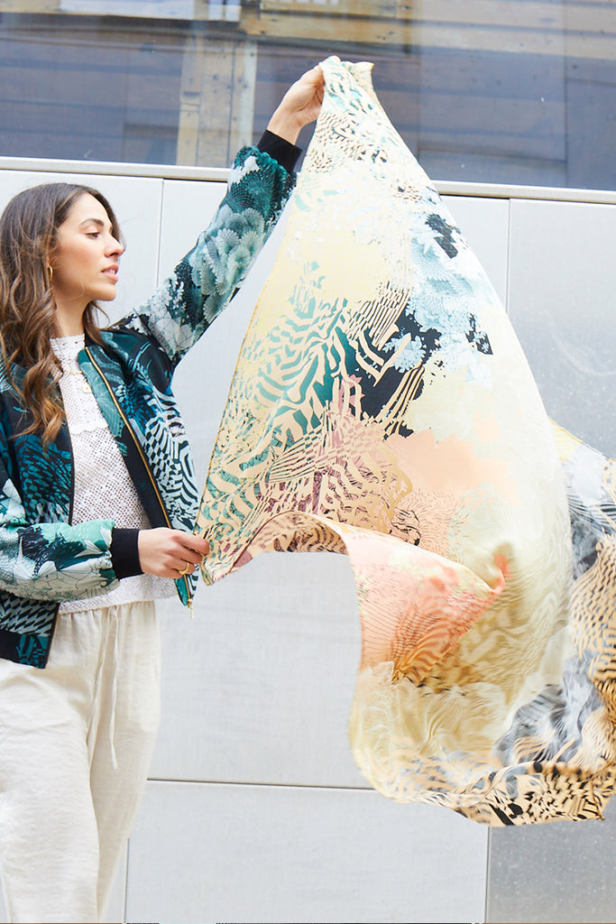 A model holding a silk scarf with a sunrise design in muted yellows, greens and coral
