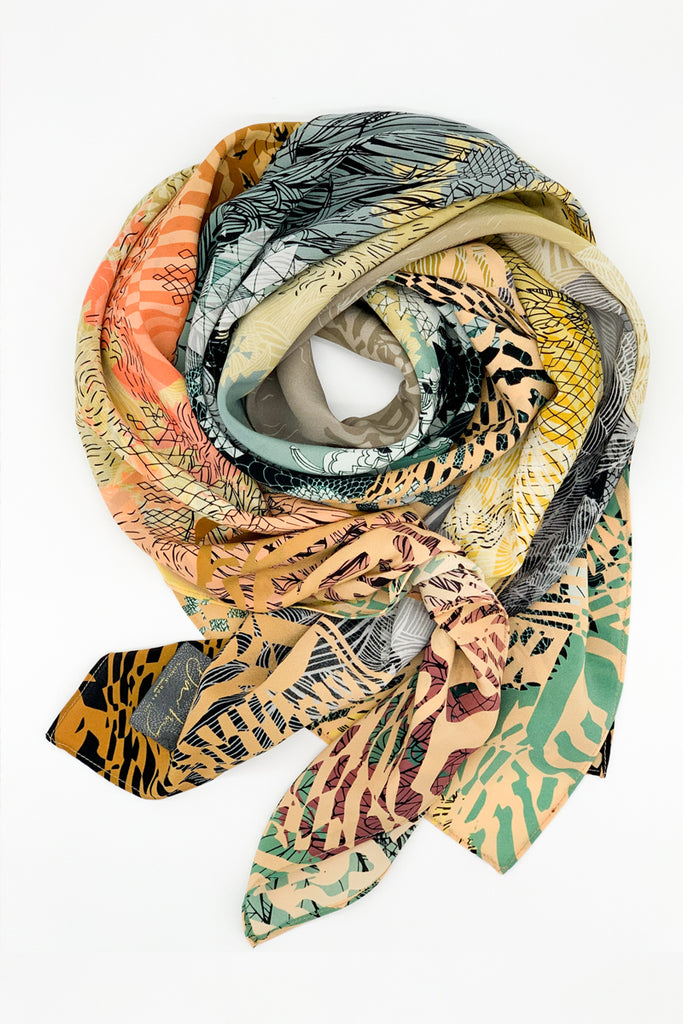A silk scarf with a sunrise design in muted yellows, greens and coral against a white background