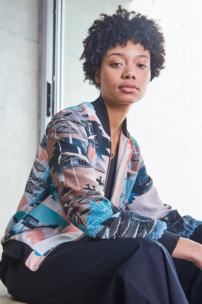 A woman wearing a printed silk bomber jacket in green, coral and browns 