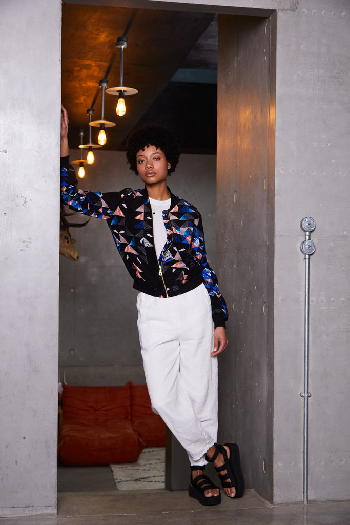 A woman wearing a silk bomber jacket with a collaged geometric print in black, blue and pink