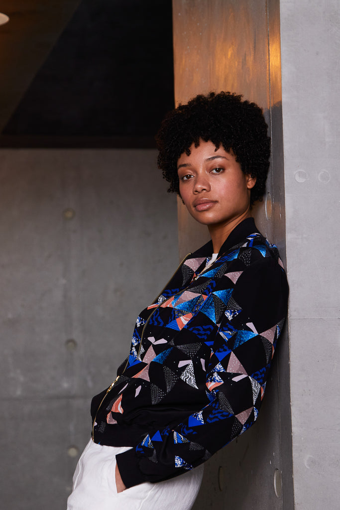 A woman wearing a silk bomber jacket with a collaged geometric print in black, blue and pink