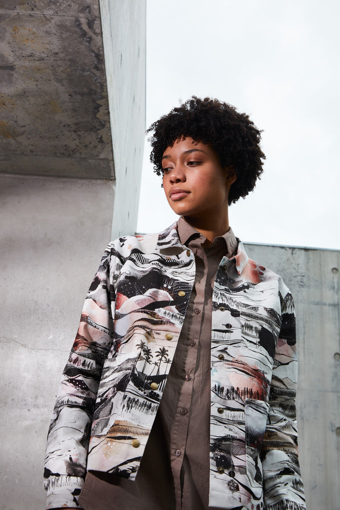 A woman wearing a cotton utility jacket with a hand drawn landscape in black, white and red 