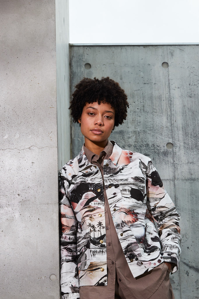 A woman wearing a cotton utility jacket with a hand drawn landscape in black, white and red 