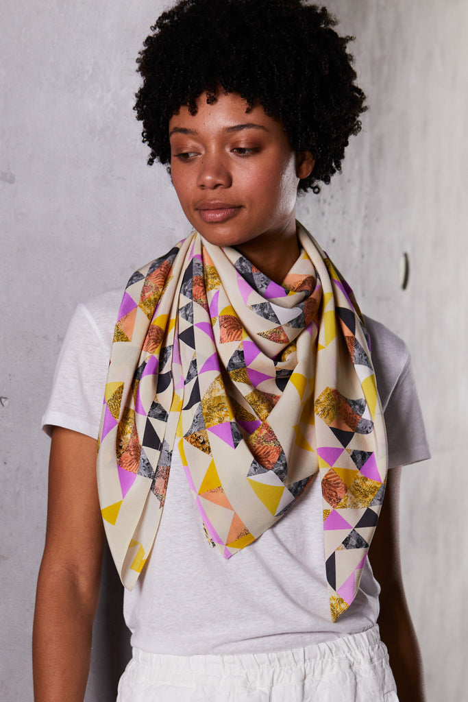 A woman wearing a silk scarf in a geometric pink and yellow print 
