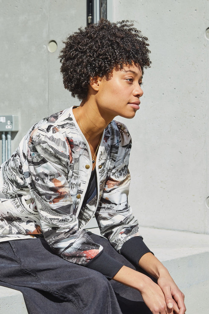 A woman wearing a cotton jacket with a landscape print in black, white and soft peachy tones