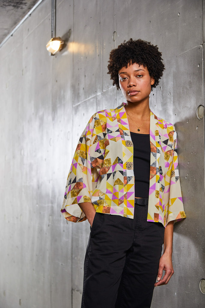 A woman wearing a short silk kimono jacket with geometric triangle print in yellow and pink